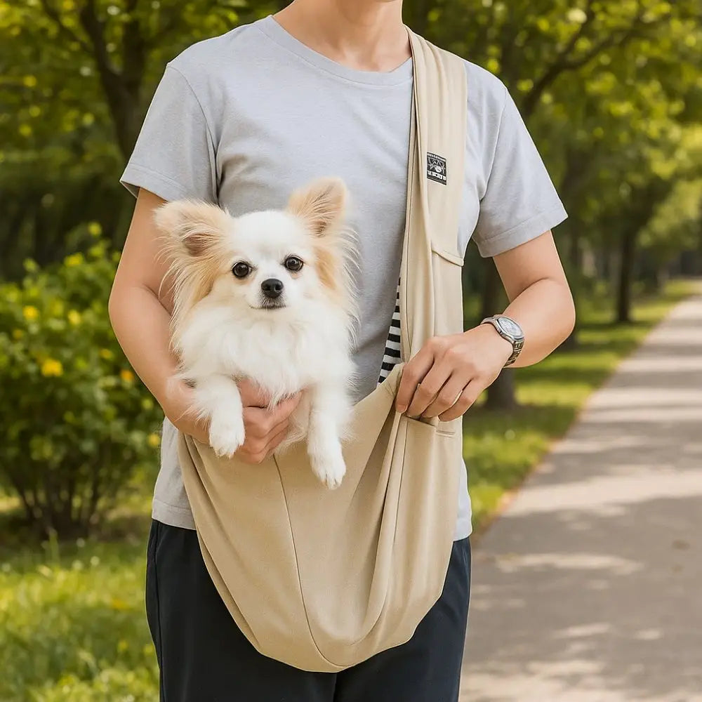 Person holding a small dog in a beige sling with a park background
